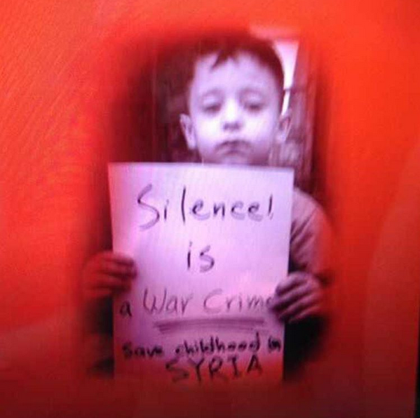 طفل سوري يحمل لافتة يستنجد بها العالم