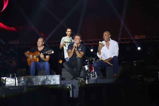 عمرو دياب يجلس على المسرح برفقة فرقته الموسيقية
